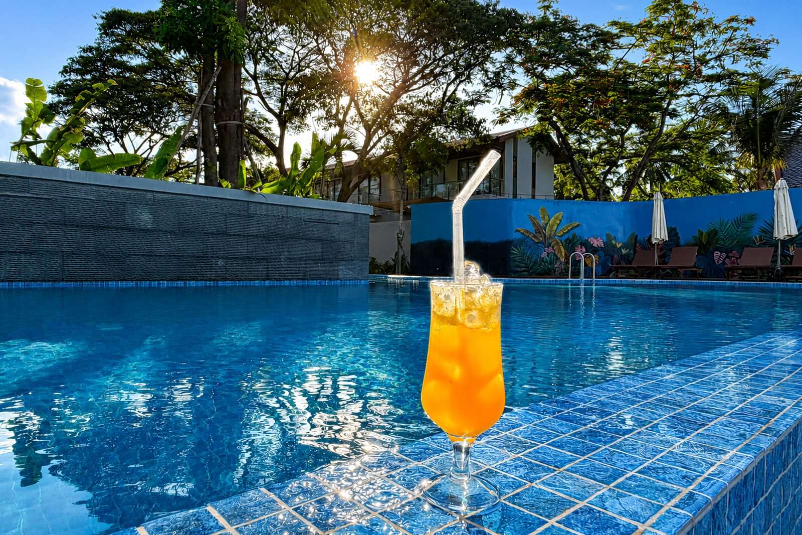 A cold drink on the pool edge with sun breaking through the trees